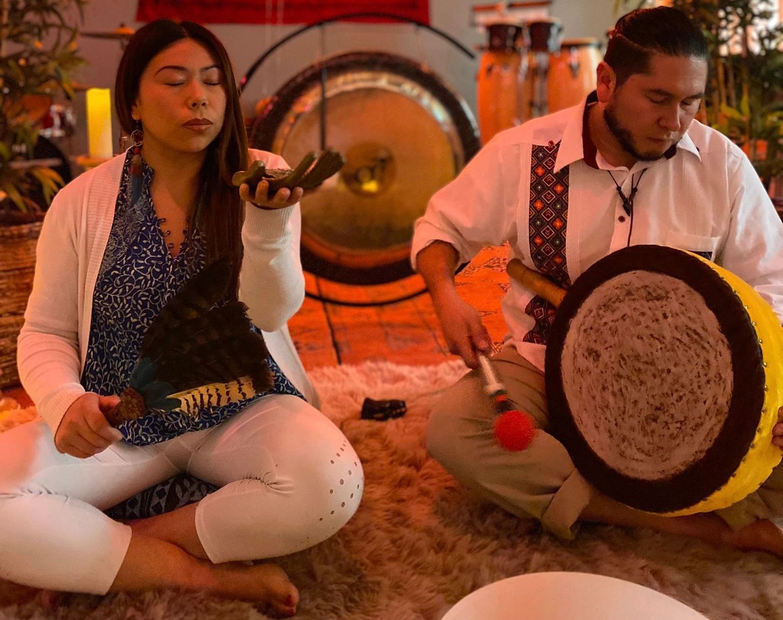 Two practitioners with drums and gong in a warm spiritual ceremony space